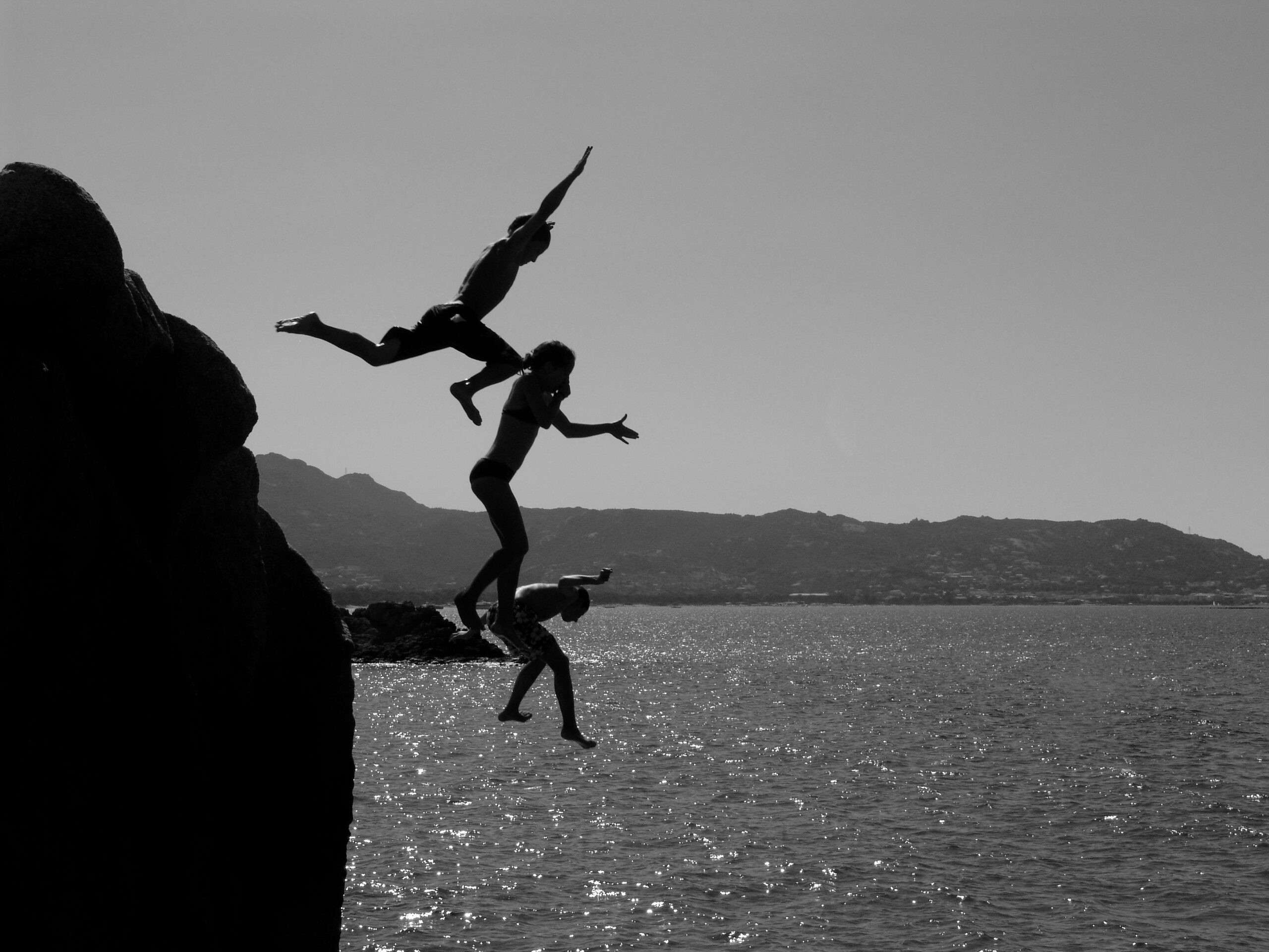 Group of kids jumping off of cliff into water